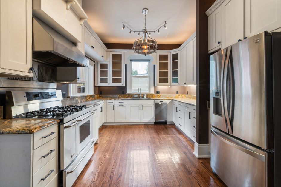 A modern white kitchen featuring wooden floors, stainless steel appliances, and granite countertops.